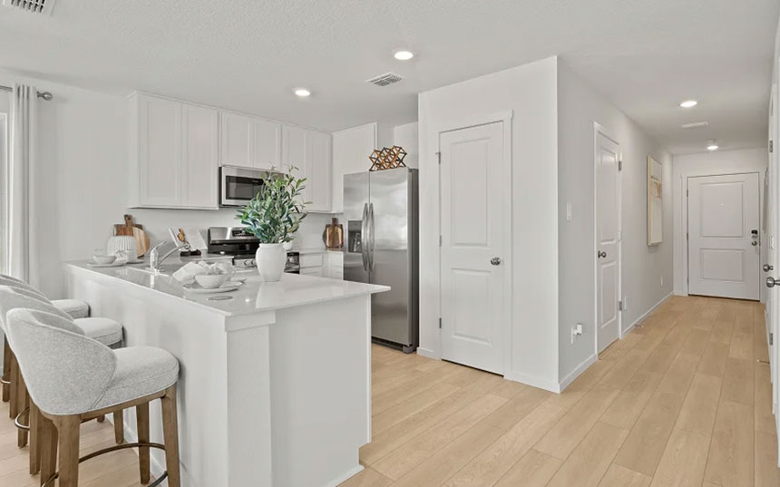 White model-home kitchen with an island, breakfast seating, and stainless-steel appliances